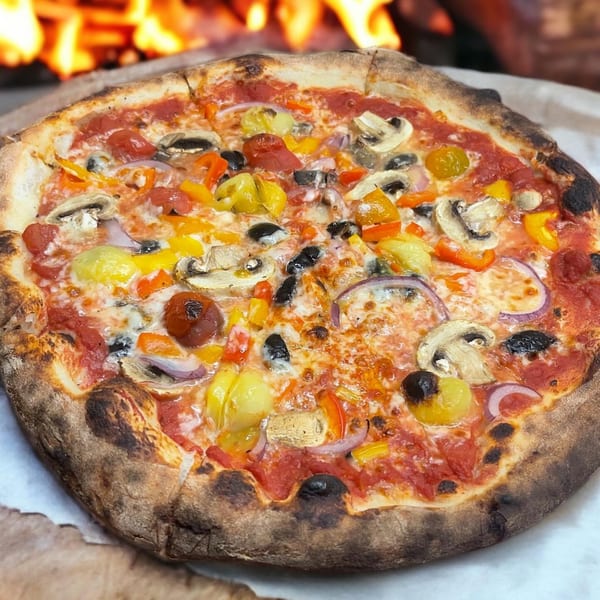 Crab Rock PIZZA's wood-fired pizza with colorful vegetables and mushrooms, against a fiery oven background.
