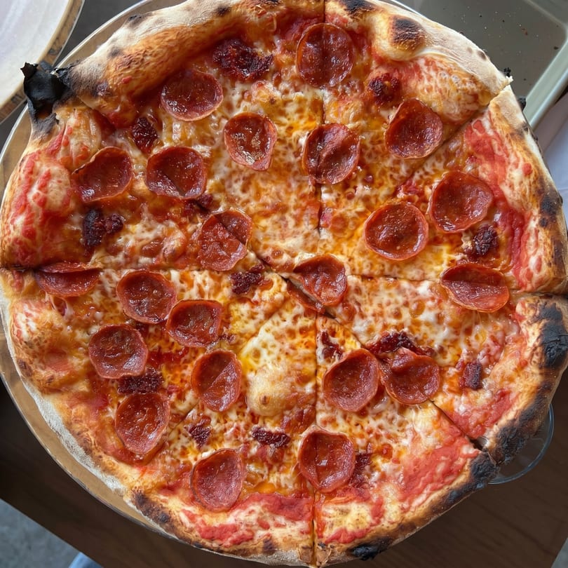 Close-up overhead view of a whole pepperoni pizza with a charred crust, sliced into eight pieces.